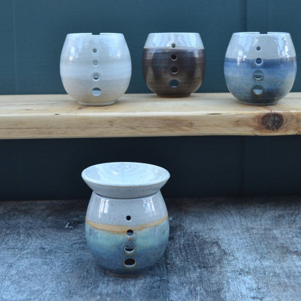 Three ceramic oil burners on a wooden surface with a dark background