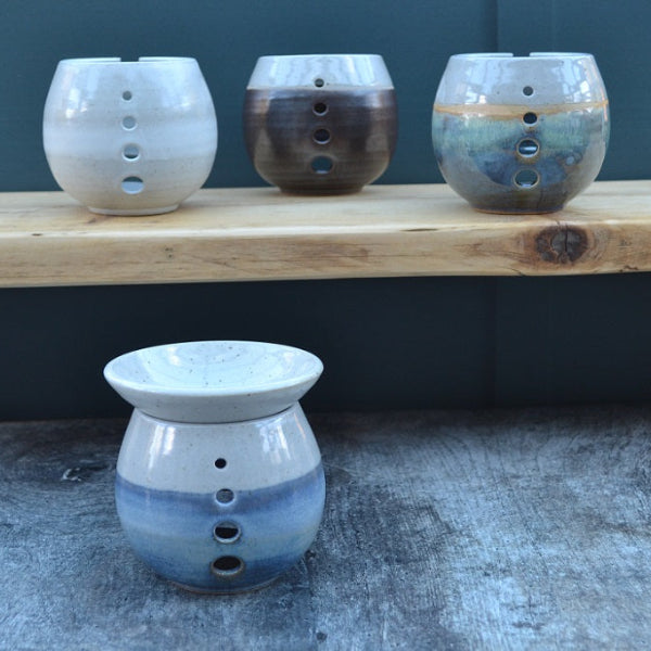 Three ceramic oil burners on a wooden shelf with a fourth one in front.