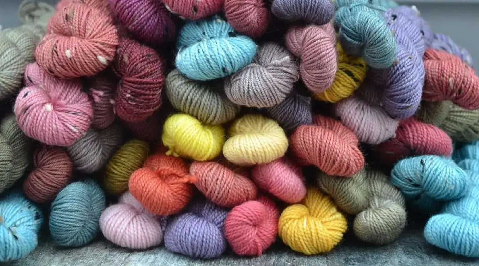 Hand dyed yarn dyed only with natural dyes. Assorted colourful yarn skeins on a textured surface