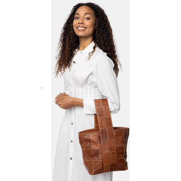 Redesigned Project 81 Torn and Cut Bag - Walnut. Woman holding a brown leather patchwork tote bag against a white background