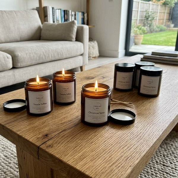 TirGlas Candles - Four lit amber glass jar candles with black lids are arranged on a wooden coffee table in a bright living room.