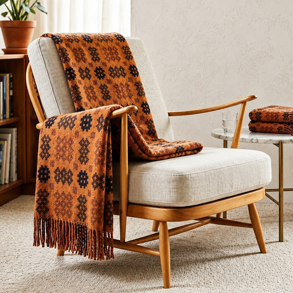 Welsh blanket named Pierhead. Patterned orange blanket draped over a wooden armchair in a cosy living room.