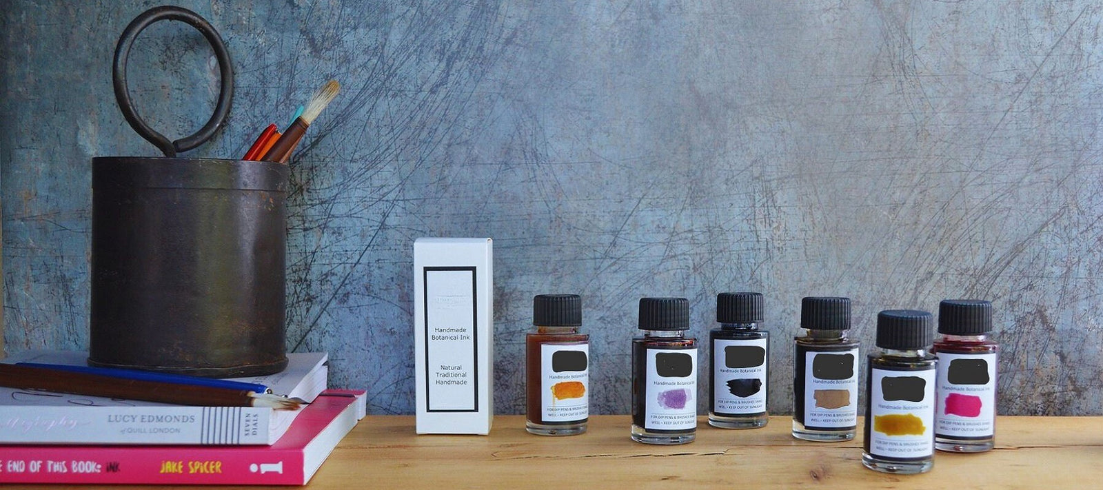 Handmade botanical inks, Oak Gall and Walnut Inks, in a set of ink bottles on a wooden surface with a textured grey wall background