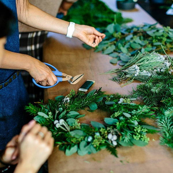 Persons arranging greenery on a table with floral shears for Christmas Wreath making workshops
