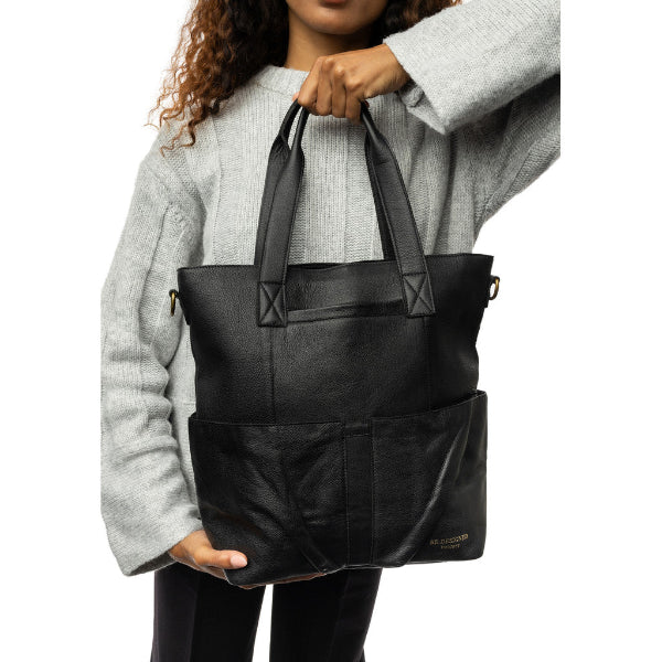 Person holding a black leather tote bag against a white background