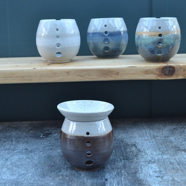 Three ceramic oil burners on a wooden surface with a fourth one on the ground.