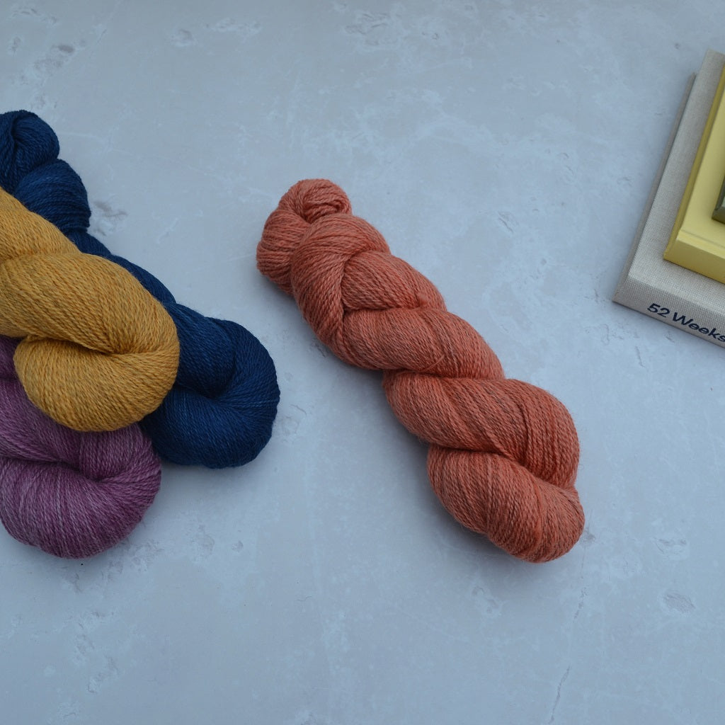 Hand dyed yarn - Three skeins of yarn in blue, yellow, and purple on a light gray surface....