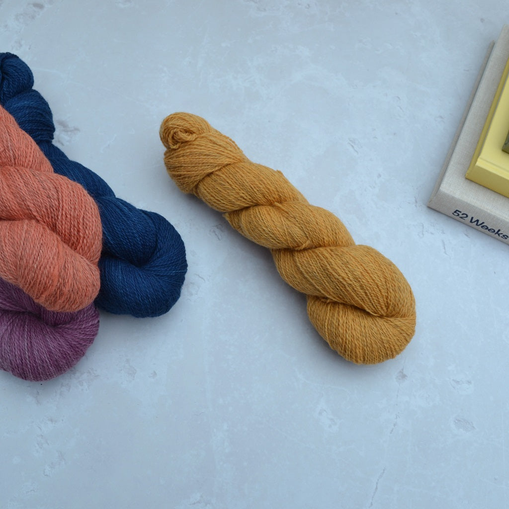 Hand dyed yarn - Three skeins of yarn in orange, blue, and purple on a light gray surface......