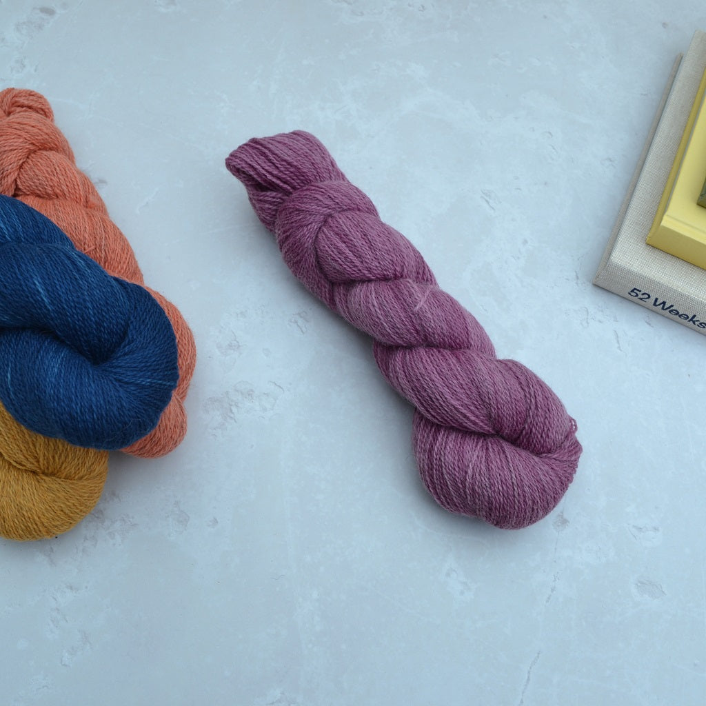 Hand dyed yarn - Three skeins of yarn in blue, orange, and purple on a light gray surface.......