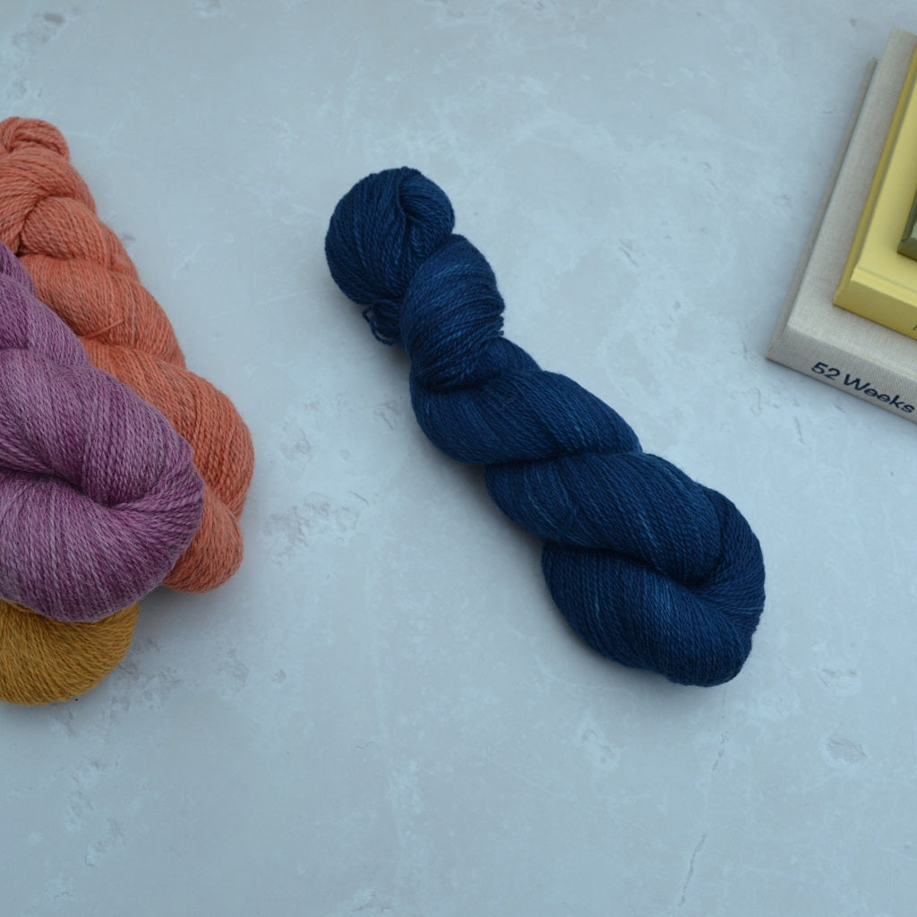 Hand dyed yarn - Three skeins of yarn in purple, orange, and blue on a light gray surface........