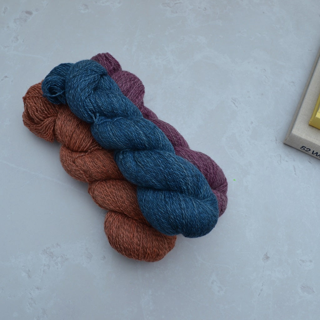Hand dyed yarn - Three skeins of yarn in blue, pink, and brown on a light gray surface.....