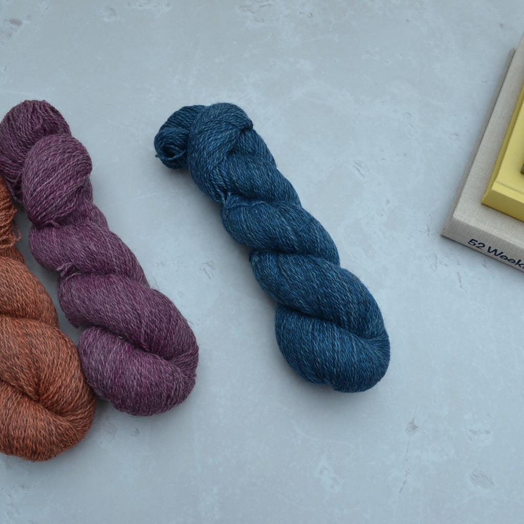Hand dyed yarn - Three skeins of yarn in purple, blue, and brown on a light gray surface...