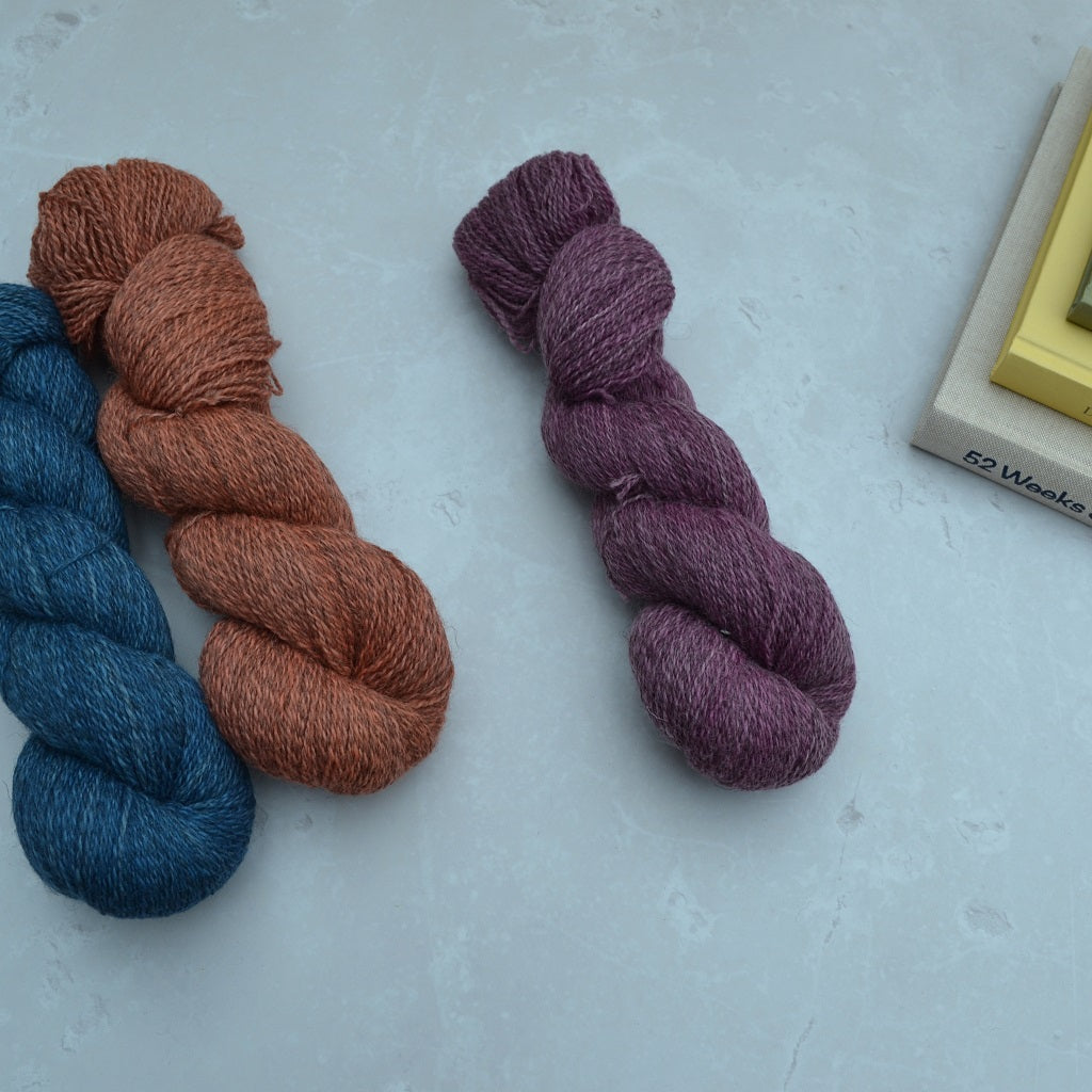 Hand dyed yarn - Three skeins of yarn in blue, brown, and purple on a light gray surface..