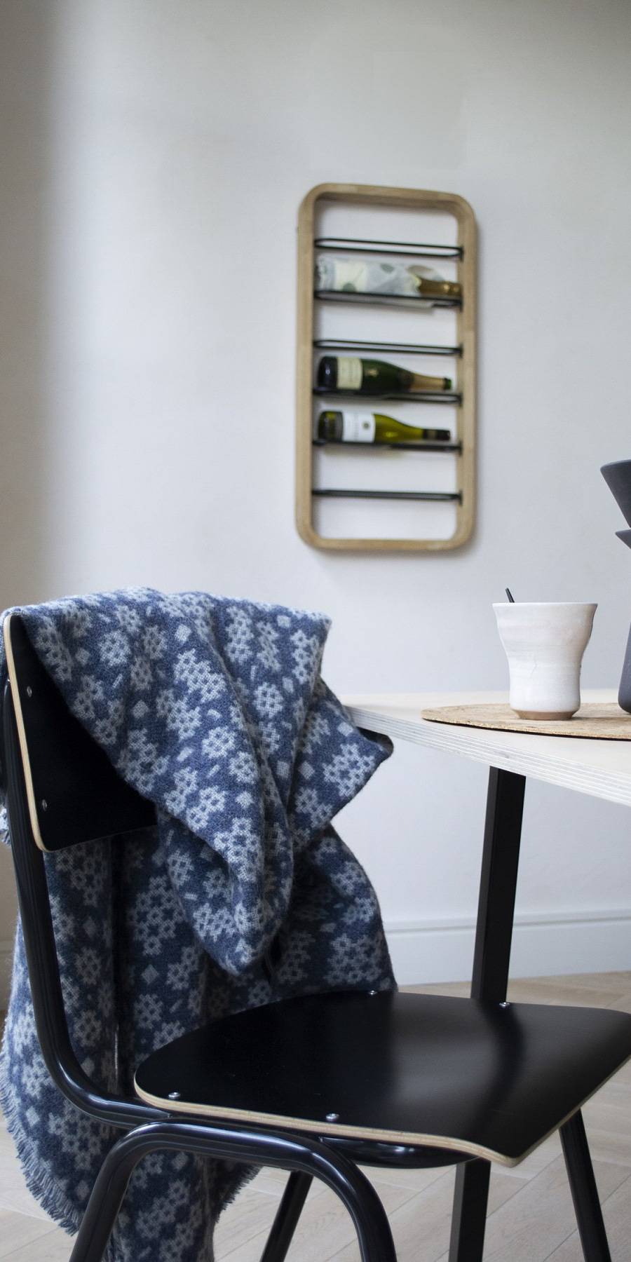 Welsh blanket. Black chair with a patterned blanket, white table with a cup, and wall-mounted shelf with bottles in a room.