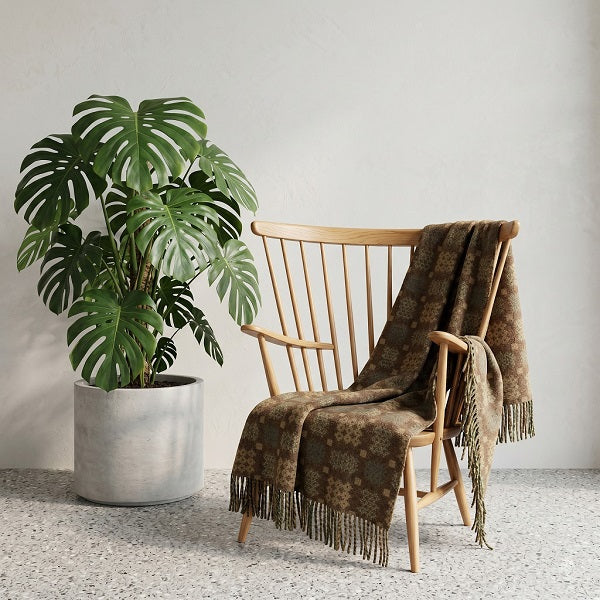 Welsh blanket named Great Orme. Wooden armchair with a brown blanket and a potted plant in a room with a light grey wall.