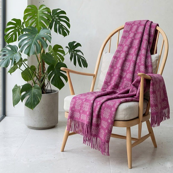 Welsh blankets named Ynys Môn. Pink patterned throw draped over a wooden chair with a plant in the background