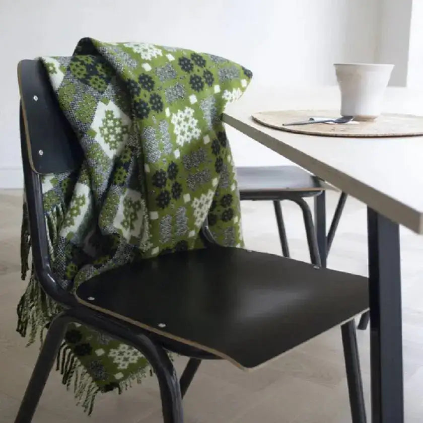 Welsh Blankets. Green patterned blanket draped over a black chair next to a dining table with a white bowl.