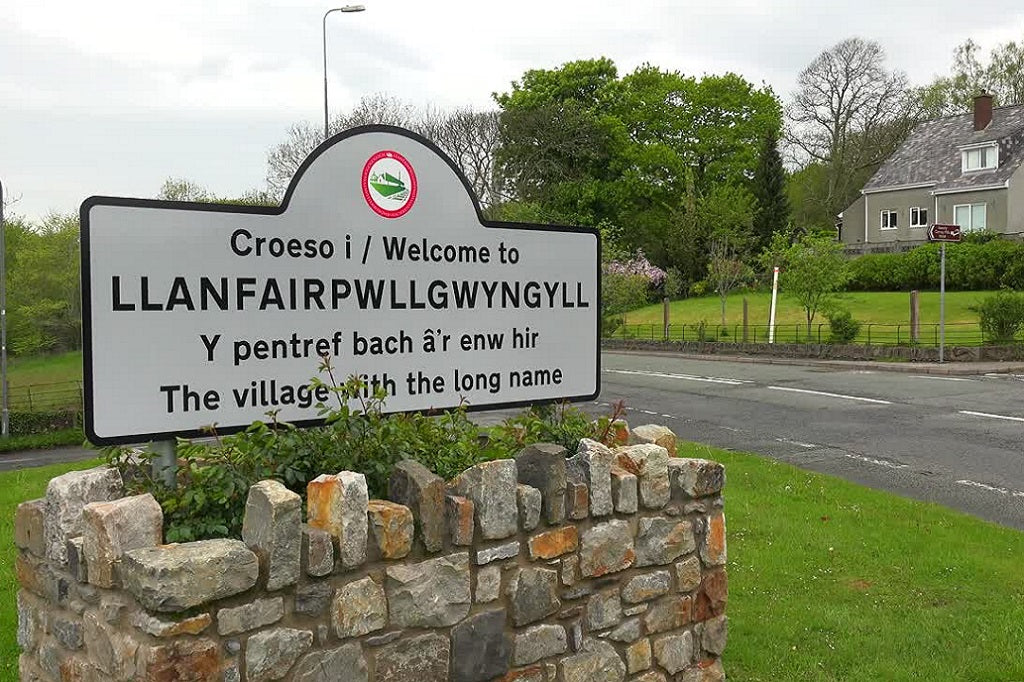 Welsh town with a long name. Welcome sign for Llanfairpwllgwyngyll with stone wall and road in background