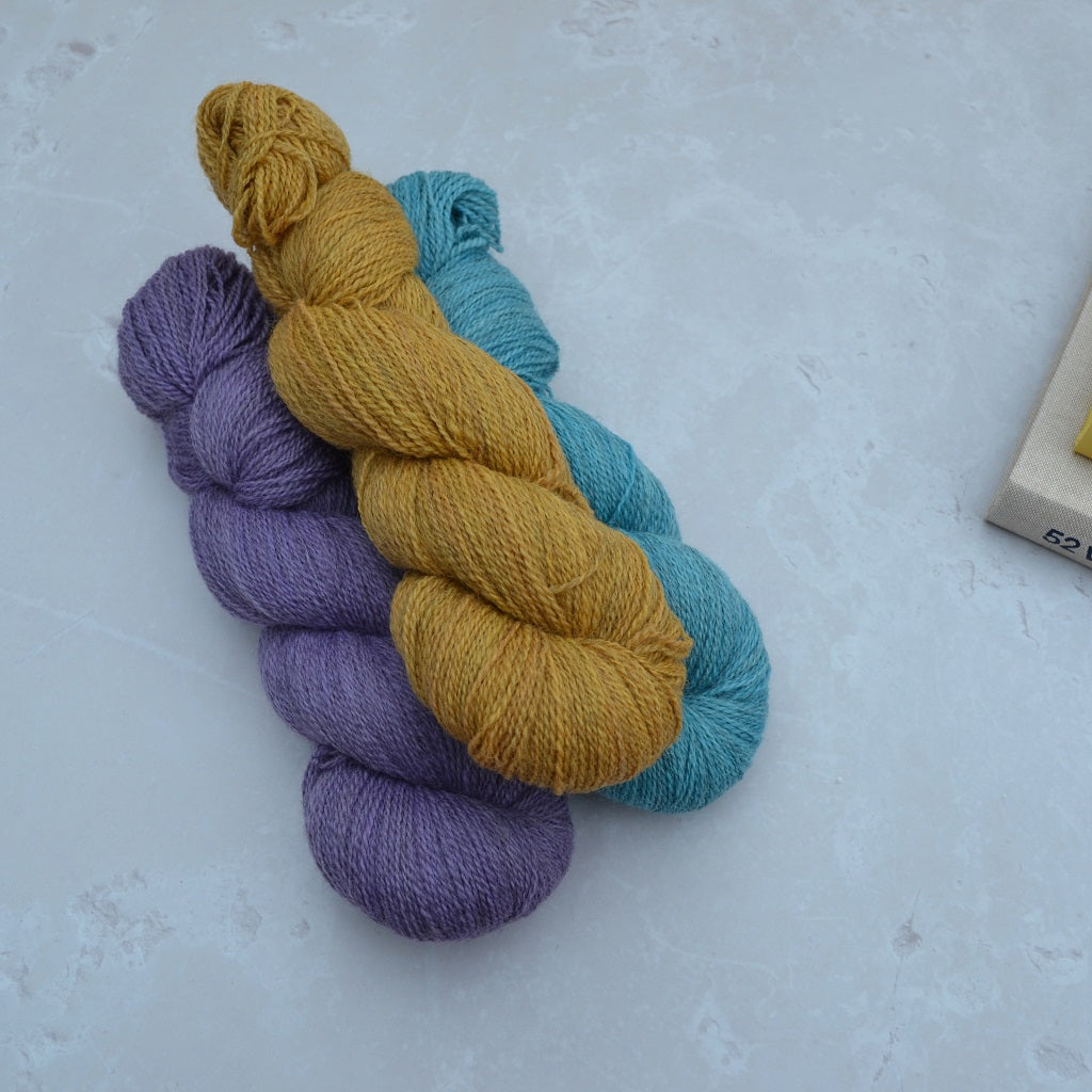 Hand dyed yarn - Three skeins of yarn in purple, yellow, and blue on a light gray background...