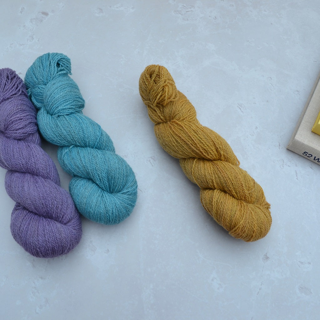 Hand dyed yarn - Three skeins of yarn in purple, blue, and yellow on a light gray background..