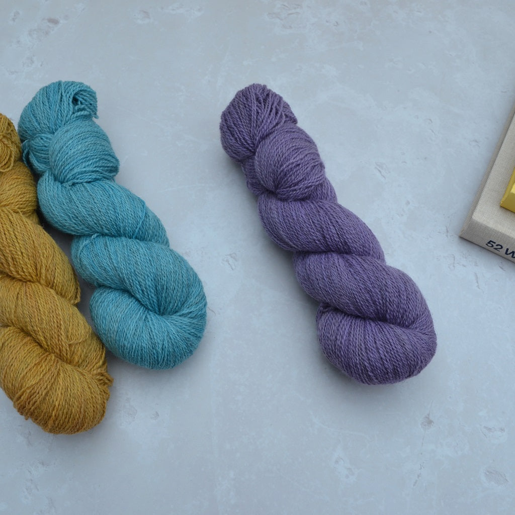Hand dyed yarn - Three skeins of yarn in yellow, blue, and purple on a light gray background.