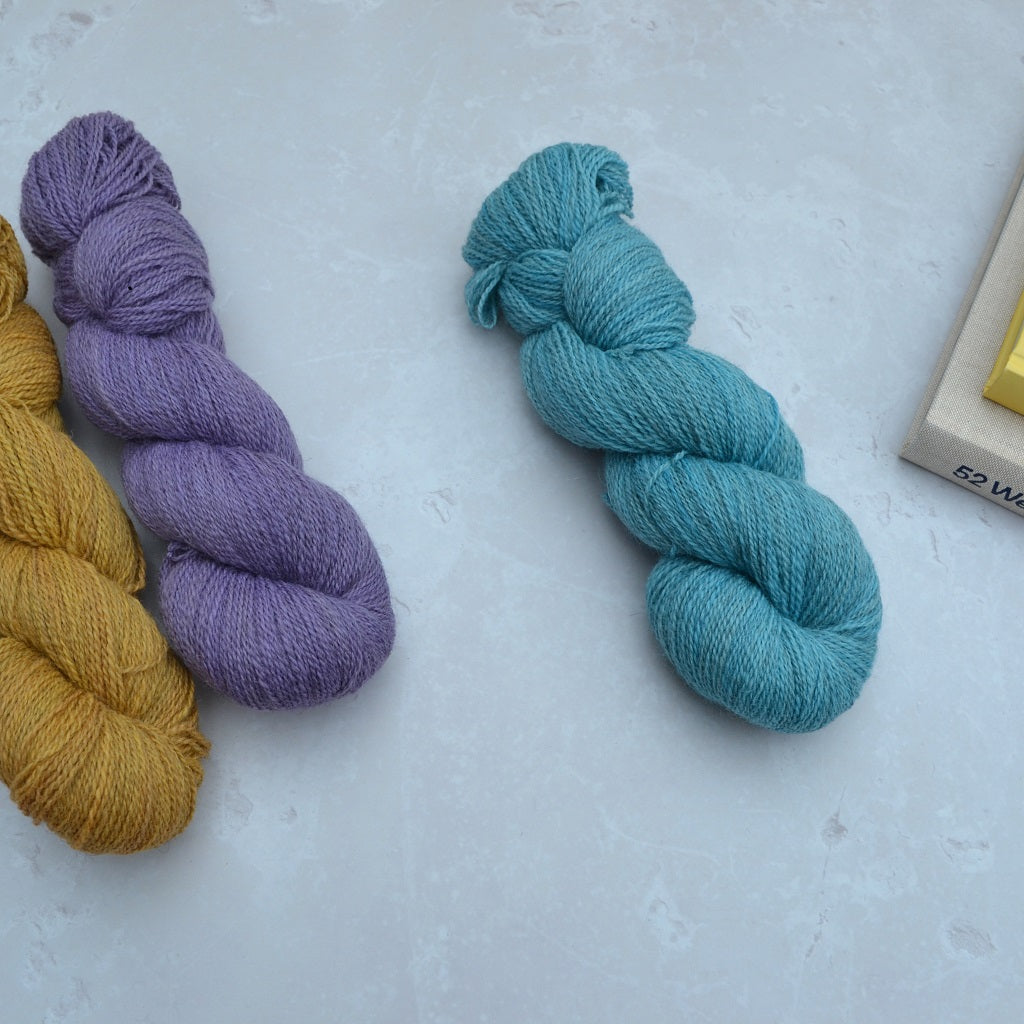 Hand dyed yarn - Three skeins of yarn in purple, yellow, and blue on a light gray surface.