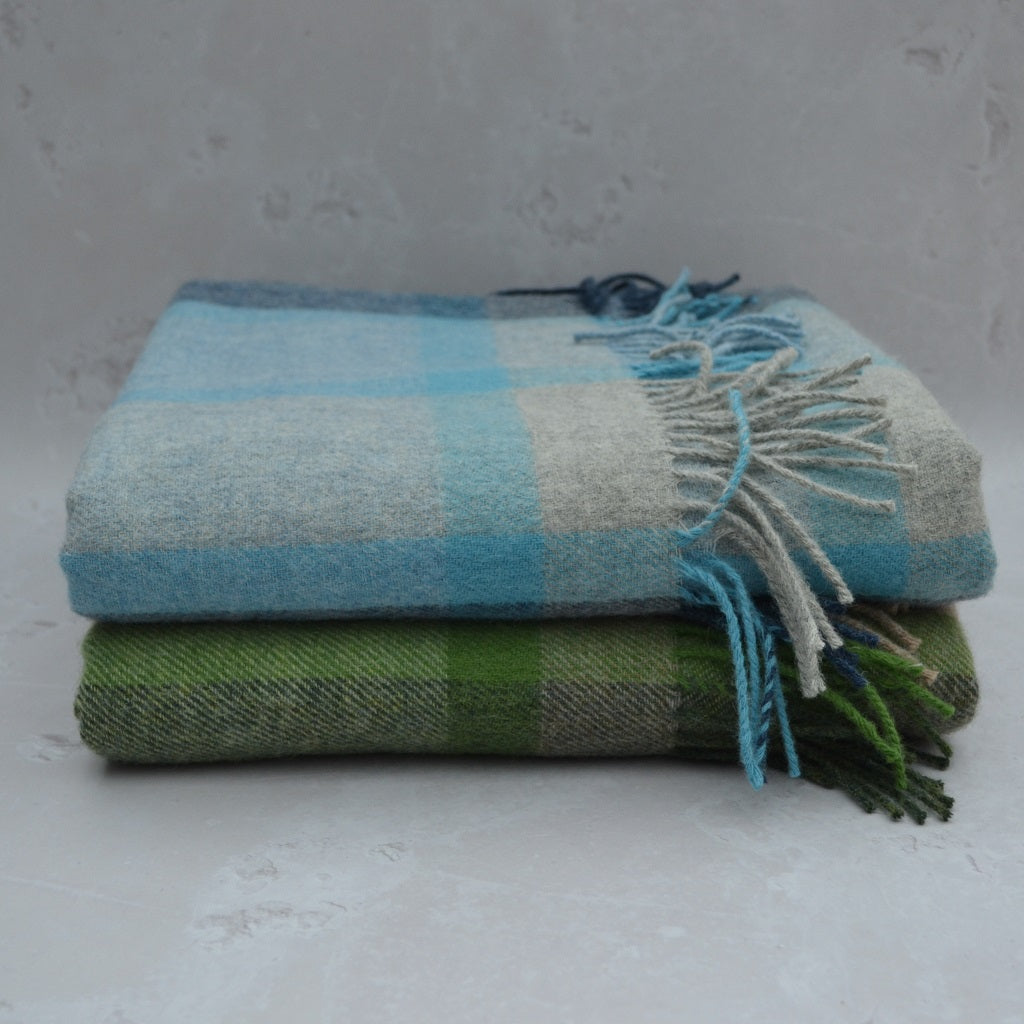 Colwyn Welsh Blanket. Stack of checkered blankets in blue and green on a gray background