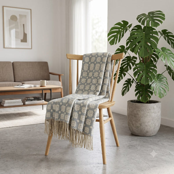 Welsh blanket named Maldwyn on a chair with a patterned blanket draped over it in a living room setting with a plant and sofa.