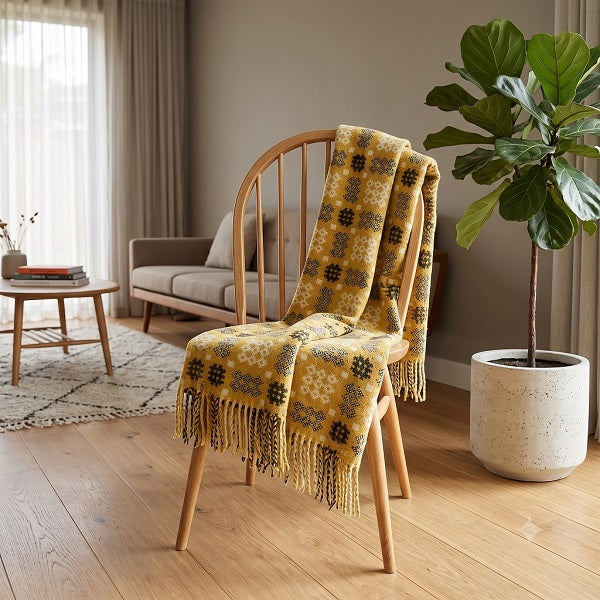 Welsh blanket named Rhondda draped over a wooden chair in  a modern living room. Yellow/amber/gold blanket