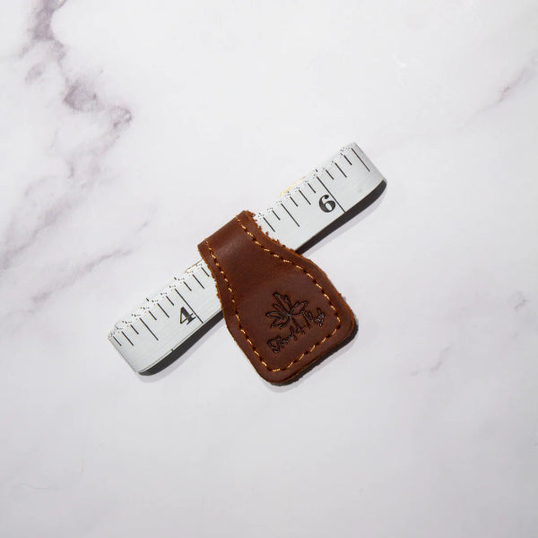 Brown leather measuring tape with a brand logo on a white marble background
